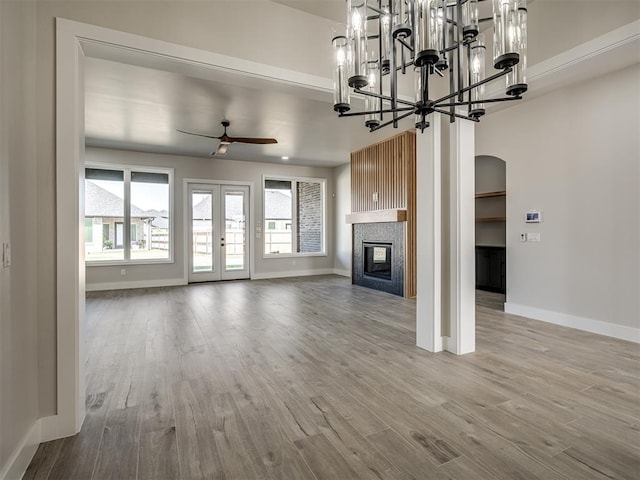 unfurnished living room with a large fireplace, ceiling fan with notable chandelier, and light wood-type flooring