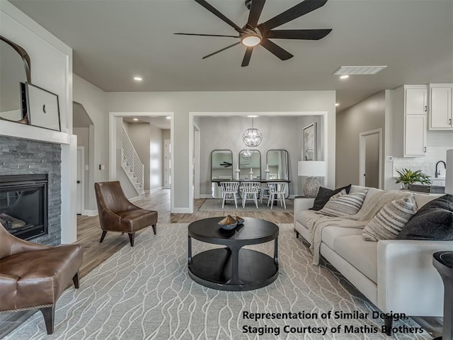 living room with a fireplace, light wood-type flooring, and ceiling fan with notable chandelier