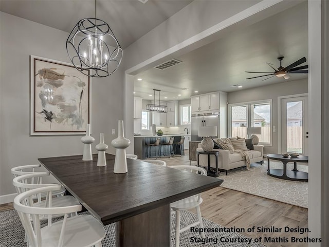 dining room with ceiling fan with notable chandelier and light hardwood / wood-style flooring