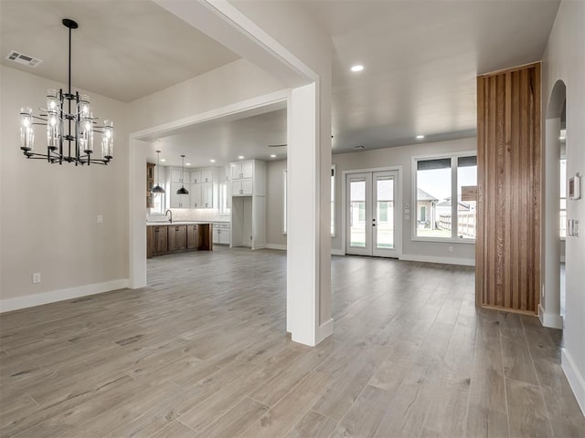 unfurnished living room with an inviting chandelier, french doors, and light hardwood / wood-style flooring