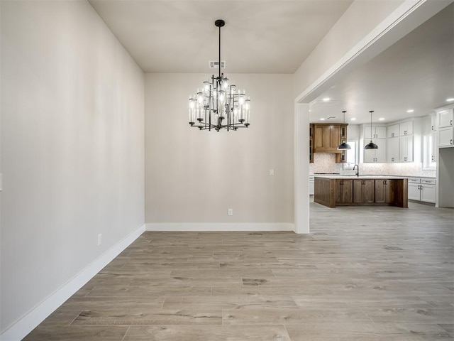 unfurnished dining area featuring sink, light hardwood / wood-style floors, and a notable chandelier