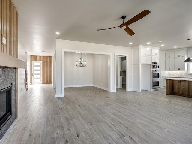 unfurnished living room featuring ceiling fan with notable chandelier, a tile fireplace, and light hardwood / wood-style flooring