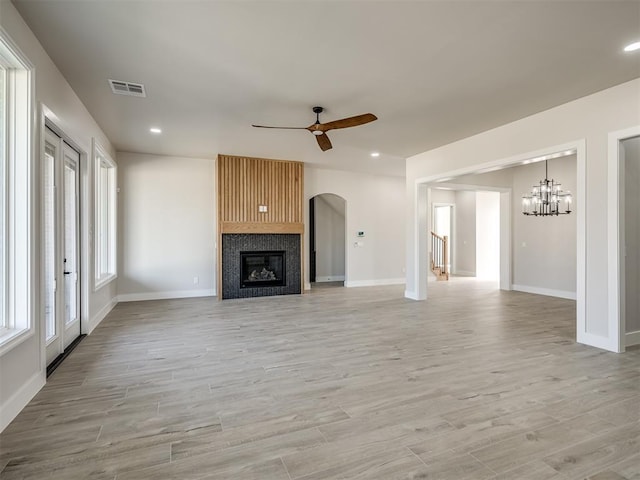 unfurnished living room featuring a fireplace, light hardwood / wood-style floors, and ceiling fan with notable chandelier