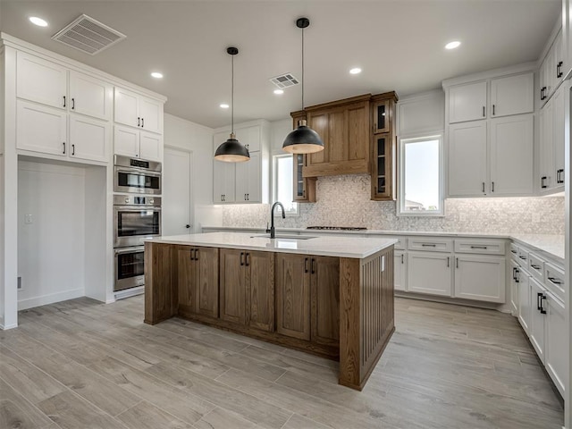 kitchen with white cabinets, sink, an island with sink, and pendant lighting