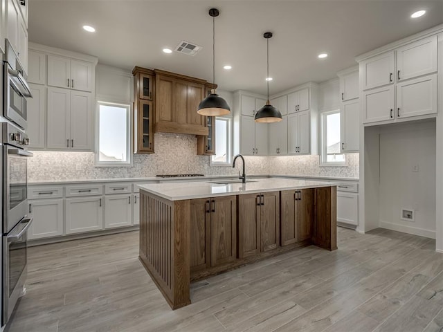 kitchen featuring white cabinetry, a kitchen island with sink, hanging light fixtures, and light wood-type flooring