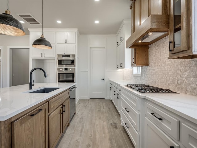 kitchen with white cabinetry, sink, stainless steel appliances, premium range hood, and decorative light fixtures