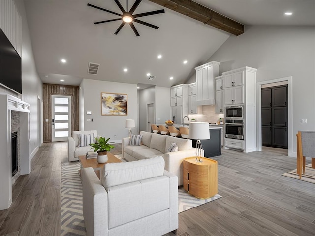 living room featuring a fireplace, high vaulted ceiling, light hardwood / wood-style floors, and beamed ceiling