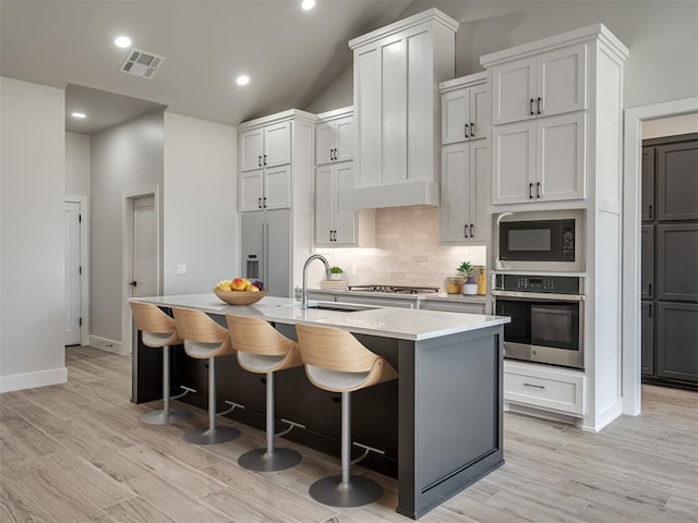 kitchen with sink, built in appliances, an island with sink, and a breakfast bar area