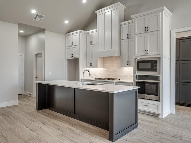 kitchen featuring sink, light hardwood / wood-style flooring, stainless steel appliances, a kitchen island with sink, and backsplash