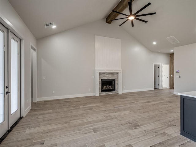 unfurnished living room with french doors, beam ceiling, a fireplace, and light hardwood / wood-style floors