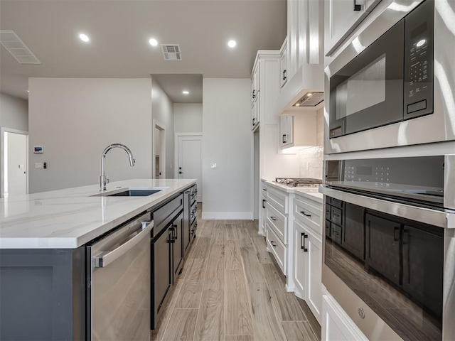 kitchen featuring sink, white cabinetry, light stone counters, a center island with sink, and appliances with stainless steel finishes