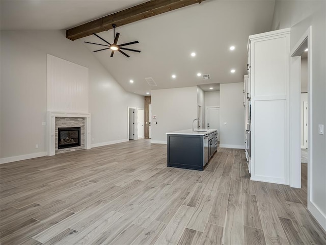 kitchen with sink, white cabinetry, vaulted ceiling with beams, a center island with sink, and a stone fireplace