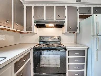 kitchen featuring black range with electric cooktop, white refrigerator, and gray cabinetry