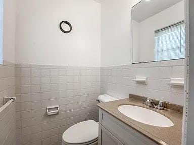 bathroom with vanity, toilet, and tile walls