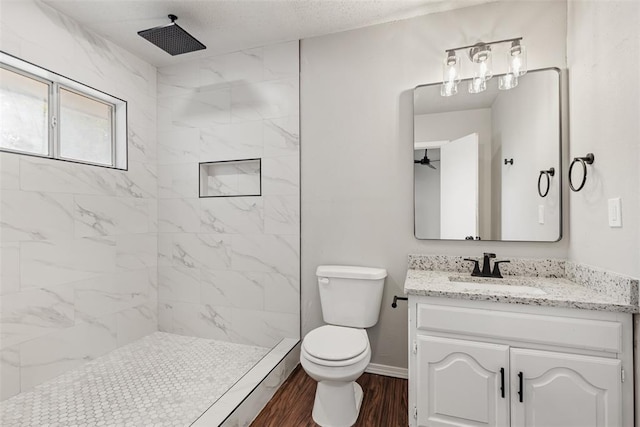 bathroom with a tile shower, vanity, wood-type flooring, and toilet