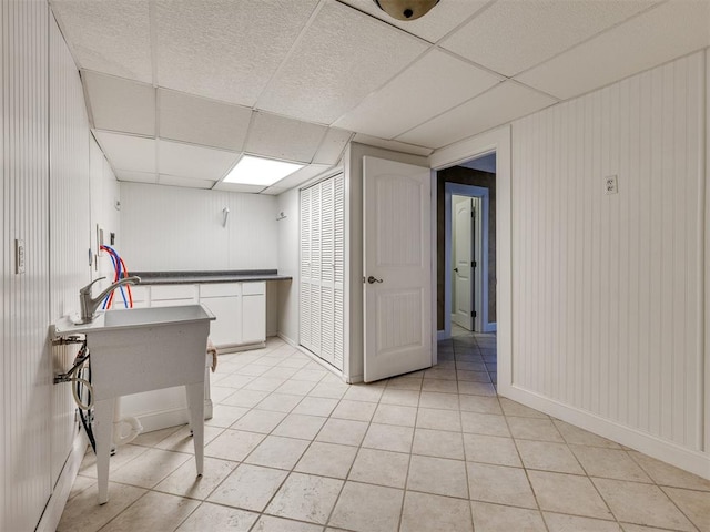 kitchen featuring a paneled ceiling, wooden walls, white cabinets, and light tile patterned flooring