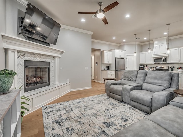 living room with a tile fireplace, ceiling fan, crown molding, and light hardwood / wood-style floors