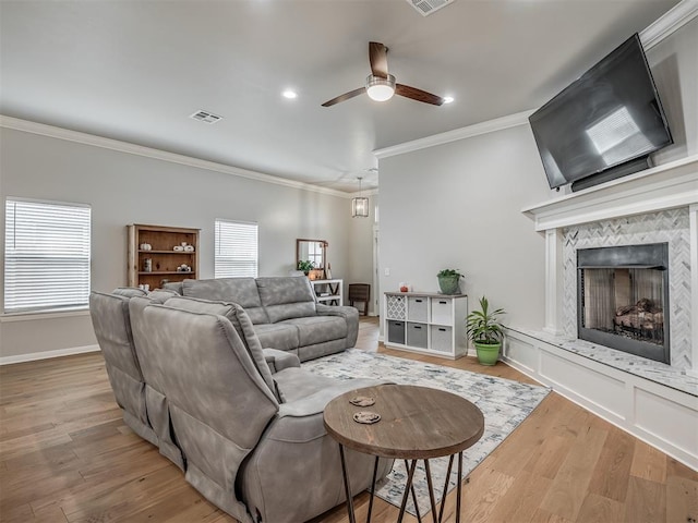 living room featuring a high end fireplace, light hardwood / wood-style flooring, ceiling fan, and ornamental molding