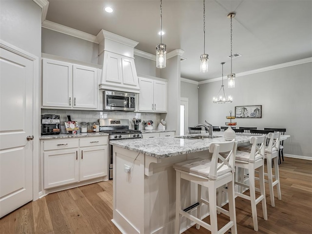 kitchen featuring a center island with sink, white cabinets, hanging light fixtures, appliances with stainless steel finishes, and light hardwood / wood-style floors