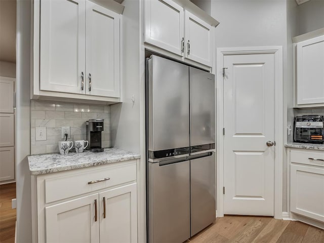 kitchen with decorative backsplash, light wood-type flooring, light stone counters, white cabinets, and stainless steel refrigerator