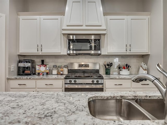 kitchen with sink, tasteful backsplash, light stone counters, white cabinetry, and stainless steel appliances