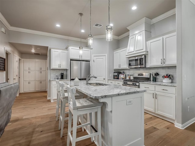 kitchen with appliances with stainless steel finishes, sink, light hardwood / wood-style floors, white cabinetry, and an island with sink