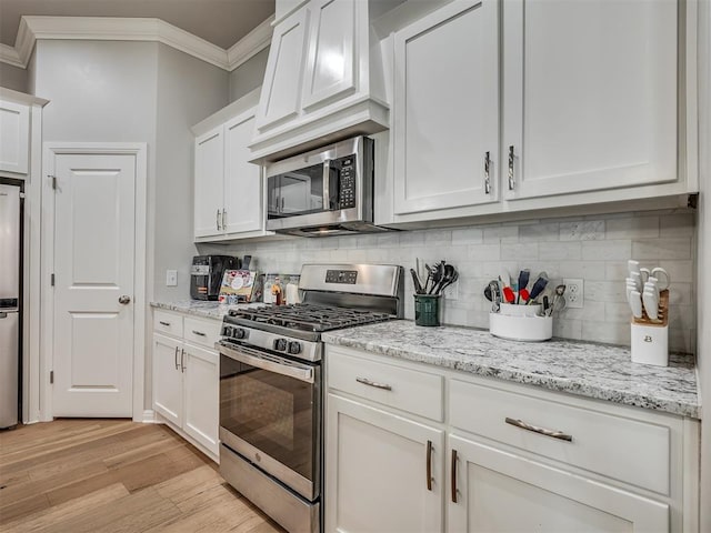 kitchen featuring white cabinets, ornamental molding, stainless steel appliances, and light hardwood / wood-style flooring