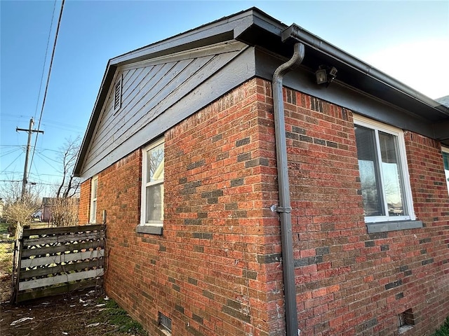 view of home's exterior with crawl space, brick siding, and fence