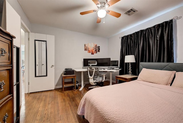 bedroom featuring a ceiling fan, wood finished floors, visible vents, and baseboards