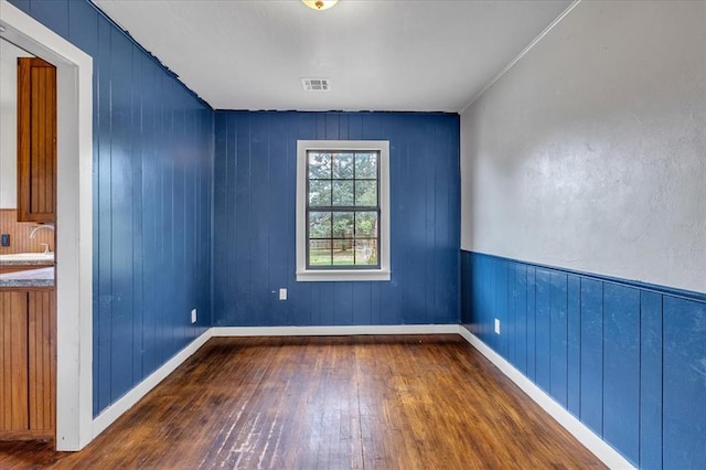 unfurnished room with dark hardwood / wood-style floors, wood walls, and sink