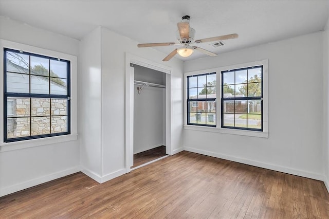 unfurnished bedroom featuring multiple windows, hardwood / wood-style floors, a closet, and ceiling fan