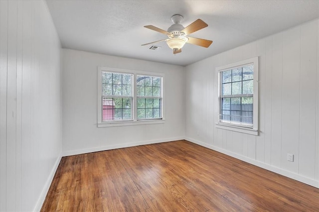 spare room featuring ceiling fan, wood walls, and hardwood / wood-style flooring