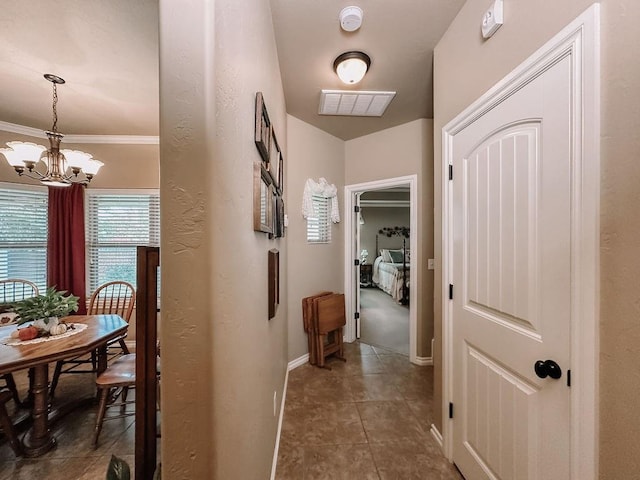 hall featuring dark tile patterned floors, crown molding, and a chandelier