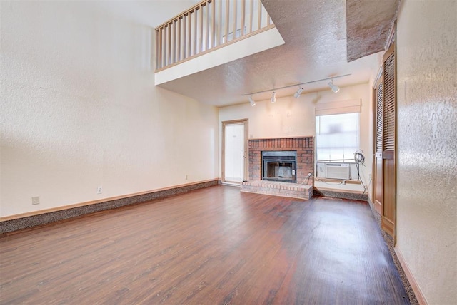 unfurnished living room featuring hardwood / wood-style floors, track lighting, cooling unit, a brick fireplace, and a textured ceiling