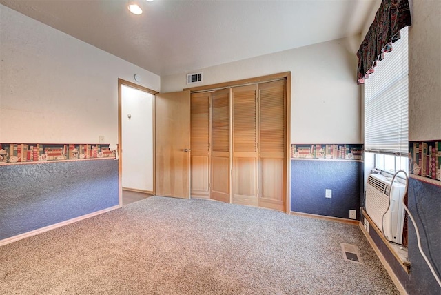 unfurnished bedroom with carpet flooring, an AC wall unit, and a closet