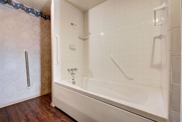 bathroom featuring wood-type flooring, tiled shower / bath combo, and a textured ceiling