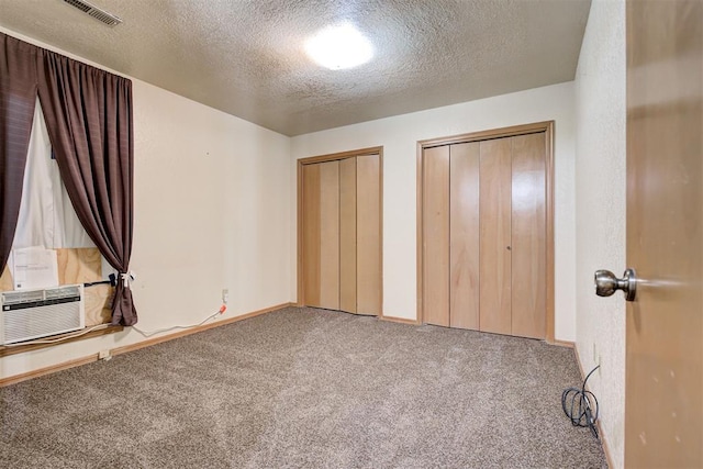 unfurnished bedroom featuring carpet, cooling unit, a textured ceiling, and multiple closets