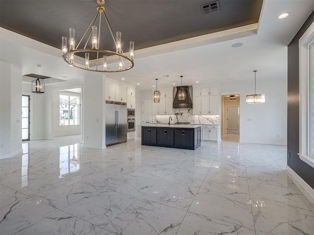 kitchen with an inviting chandelier, hanging light fixtures, a center island with sink, a tray ceiling, and white cabinets