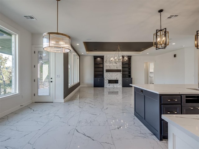 kitchen featuring an inviting chandelier, a tray ceiling, pendant lighting, a fireplace, and light stone countertops