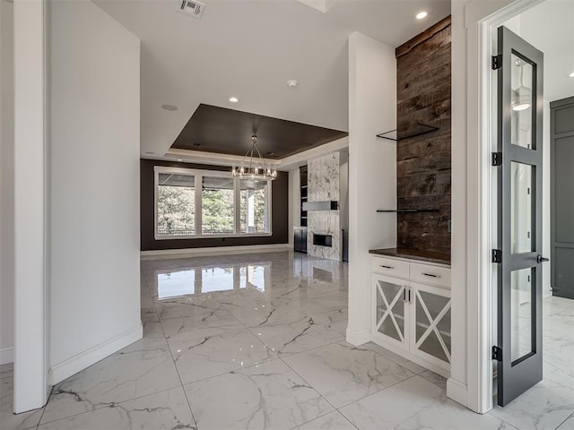 entrance foyer with a premium fireplace, a tray ceiling, and a chandelier