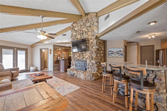 living room with vaulted ceiling with beams, wood-type flooring, a wood stove, and a textured ceiling