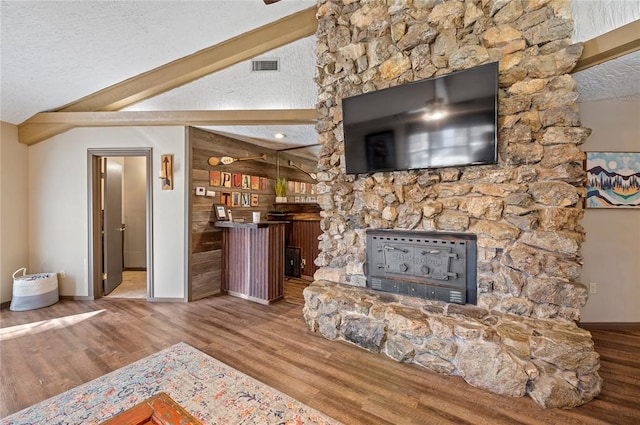 living room with vaulted ceiling with beams, wood-type flooring, a textured ceiling, and a wood stove