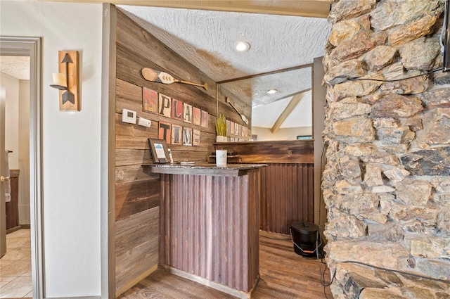 bar featuring wood walls, hardwood / wood-style floors, lofted ceiling with beams, and a textured ceiling