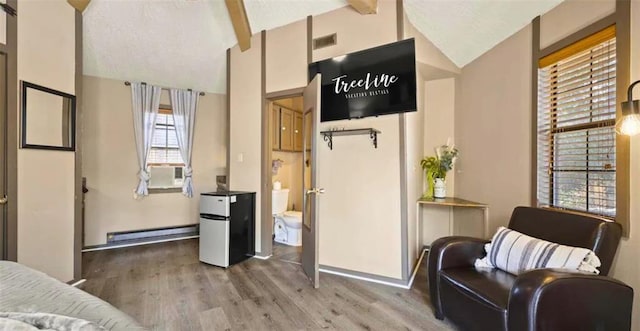 sitting room with a wealth of natural light, beamed ceiling, wood-type flooring, and a baseboard heating unit