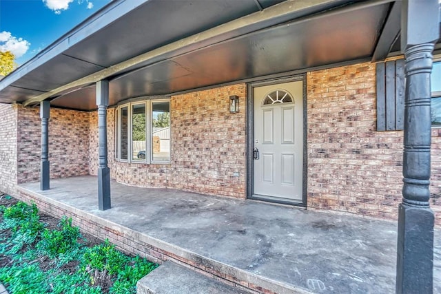 view of exterior entry featuring covered porch and brick siding