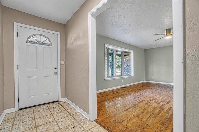 entryway with a textured ceiling, light floors, a ceiling fan, and baseboards