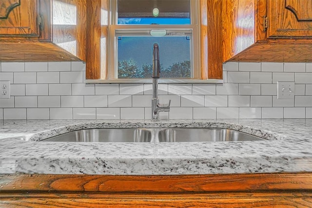 kitchen featuring light stone countertops, backsplash, brown cabinetry, and a sink