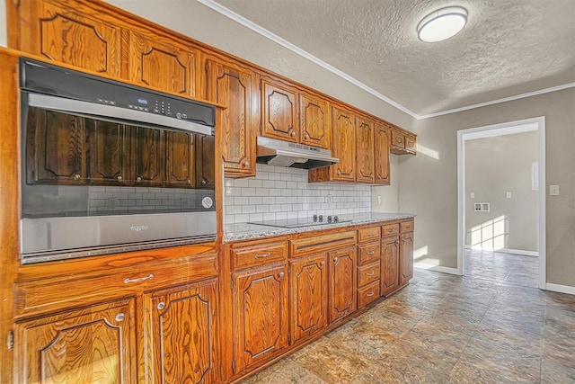 kitchen with brown cabinets, black electric stovetop, light countertops, under cabinet range hood, and stainless steel oven