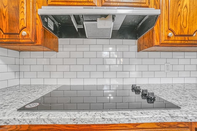 kitchen featuring brown cabinets, black electric cooktop, ventilation hood, and backsplash