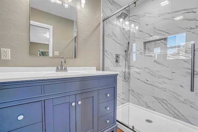 full bath with a textured wall, a marble finish shower, and vanity